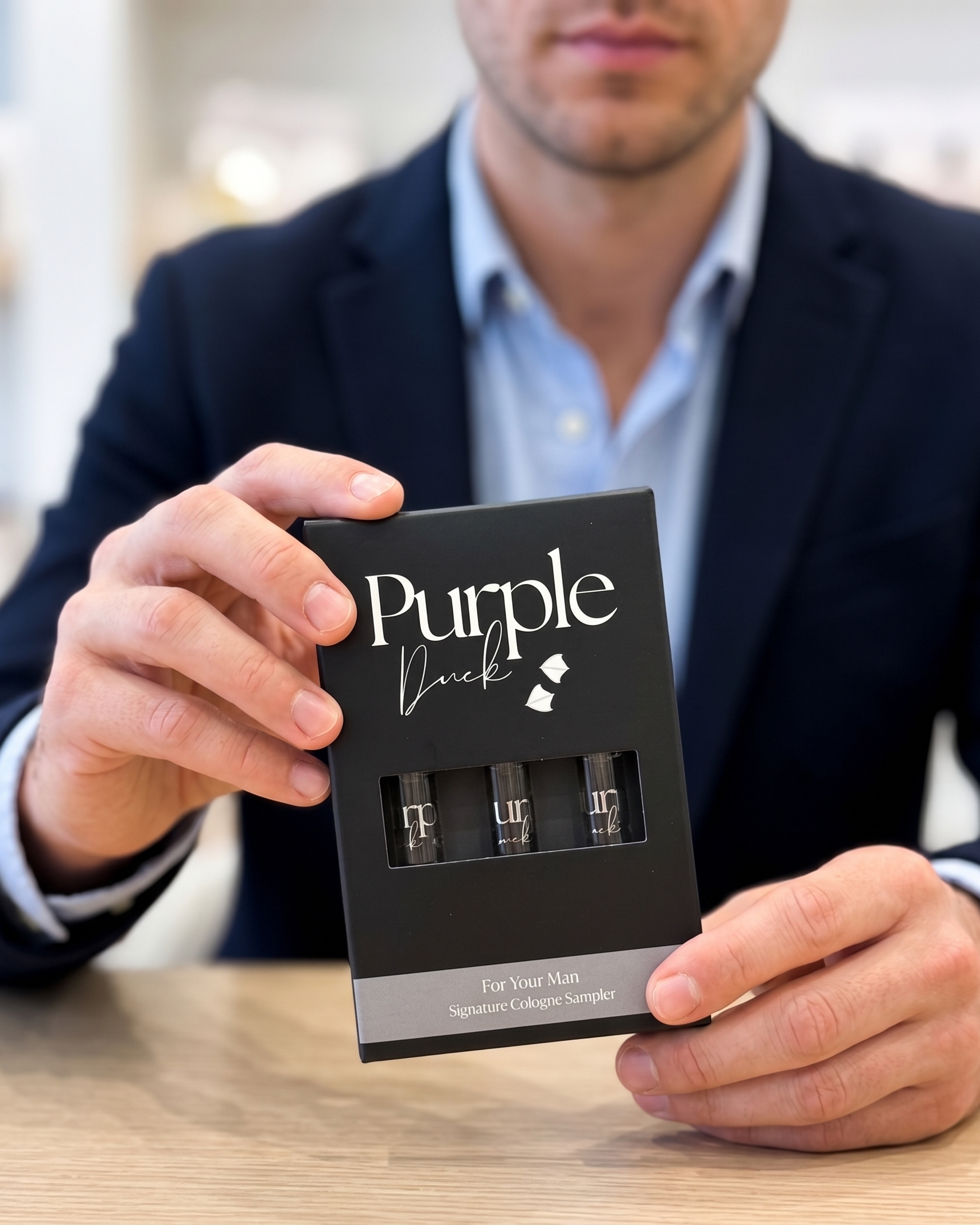 Man holding a 'Purple Duck' sample cologne pack on a wooden surface.