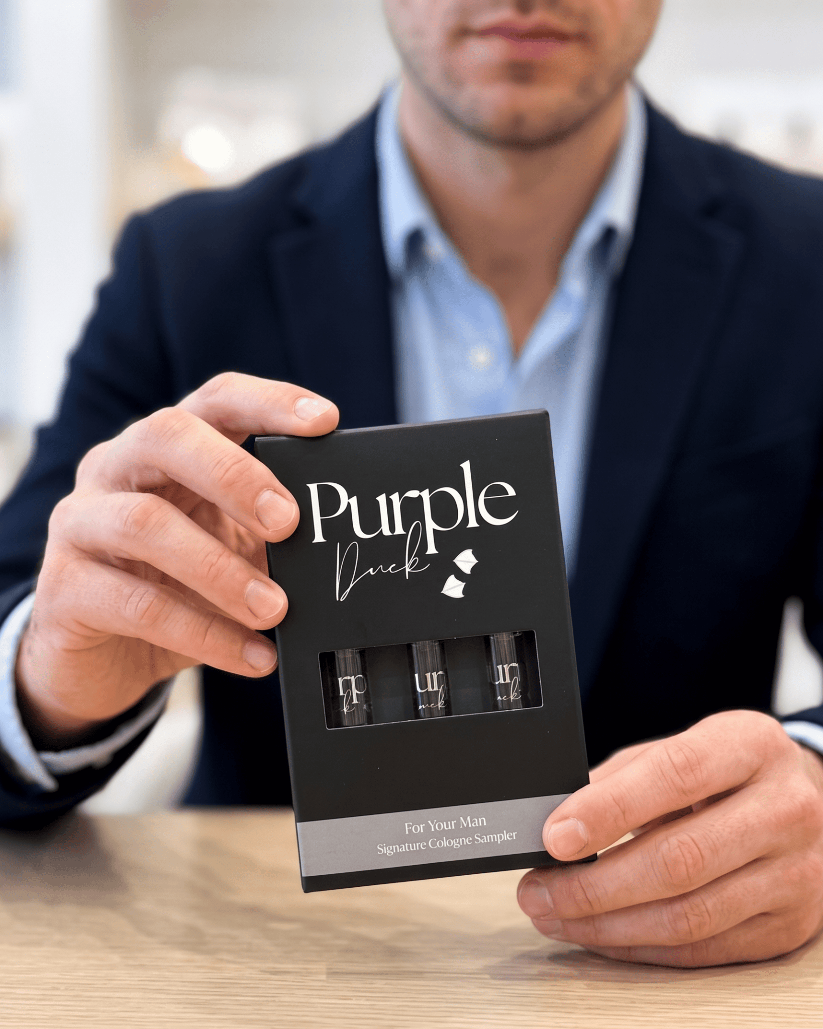 Man holding a 'Purple Duck' sample cologne pack on a wooden surface.