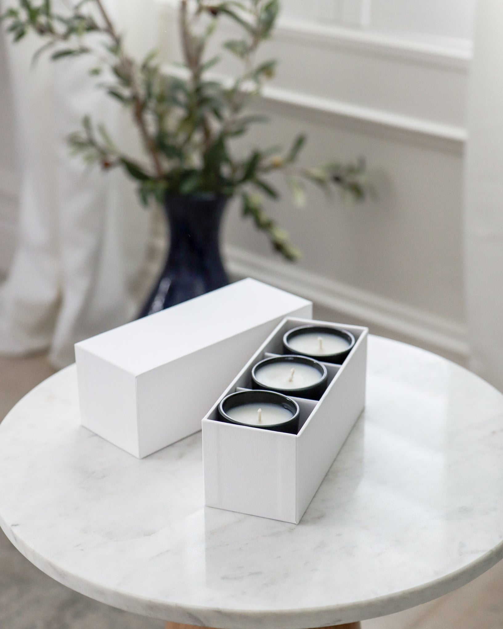 Three sample candles in a white box on a marble table with a vase of flowers in the background.