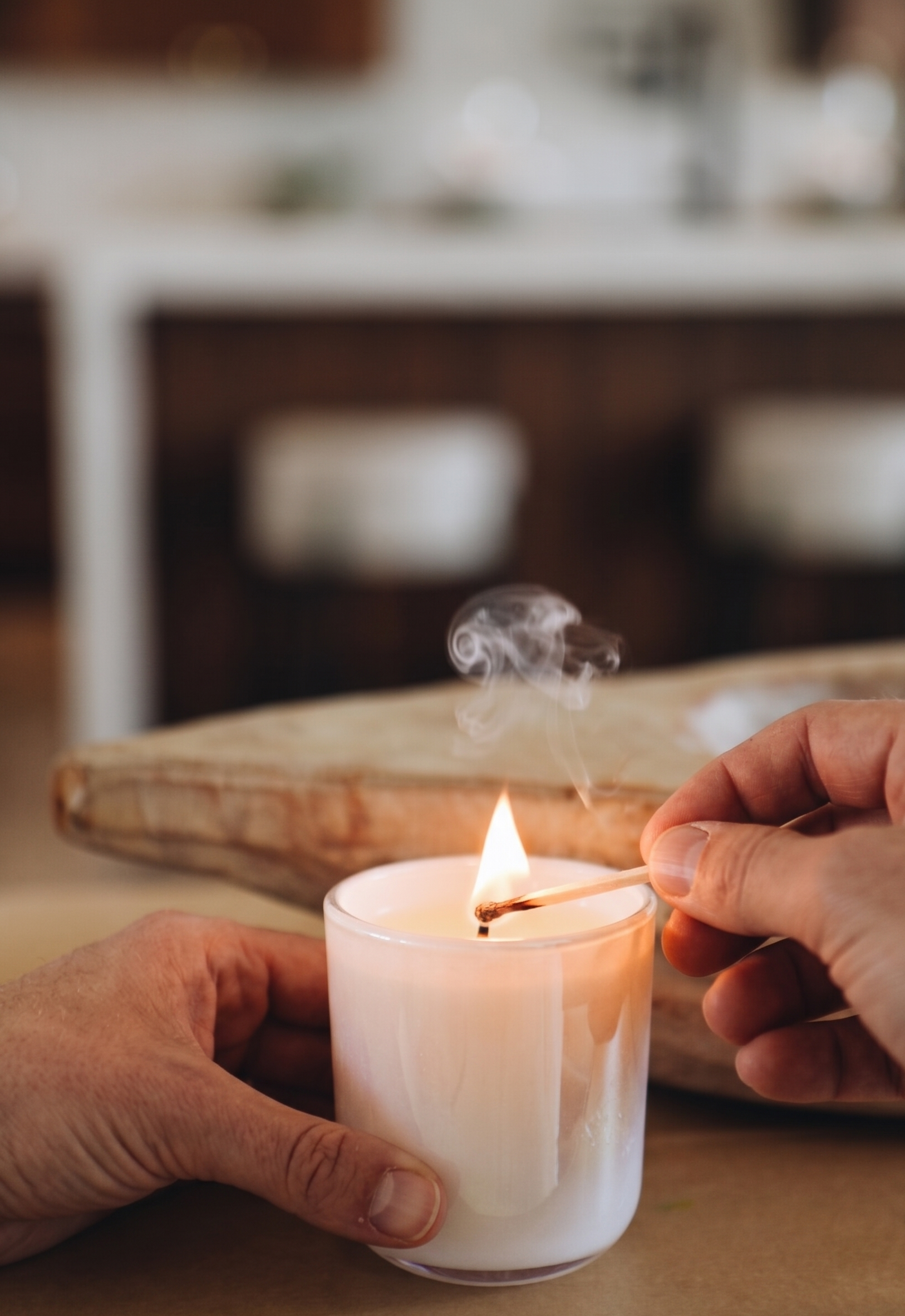 Person lighting a purple duck sample candle with a match on a wooden surface.